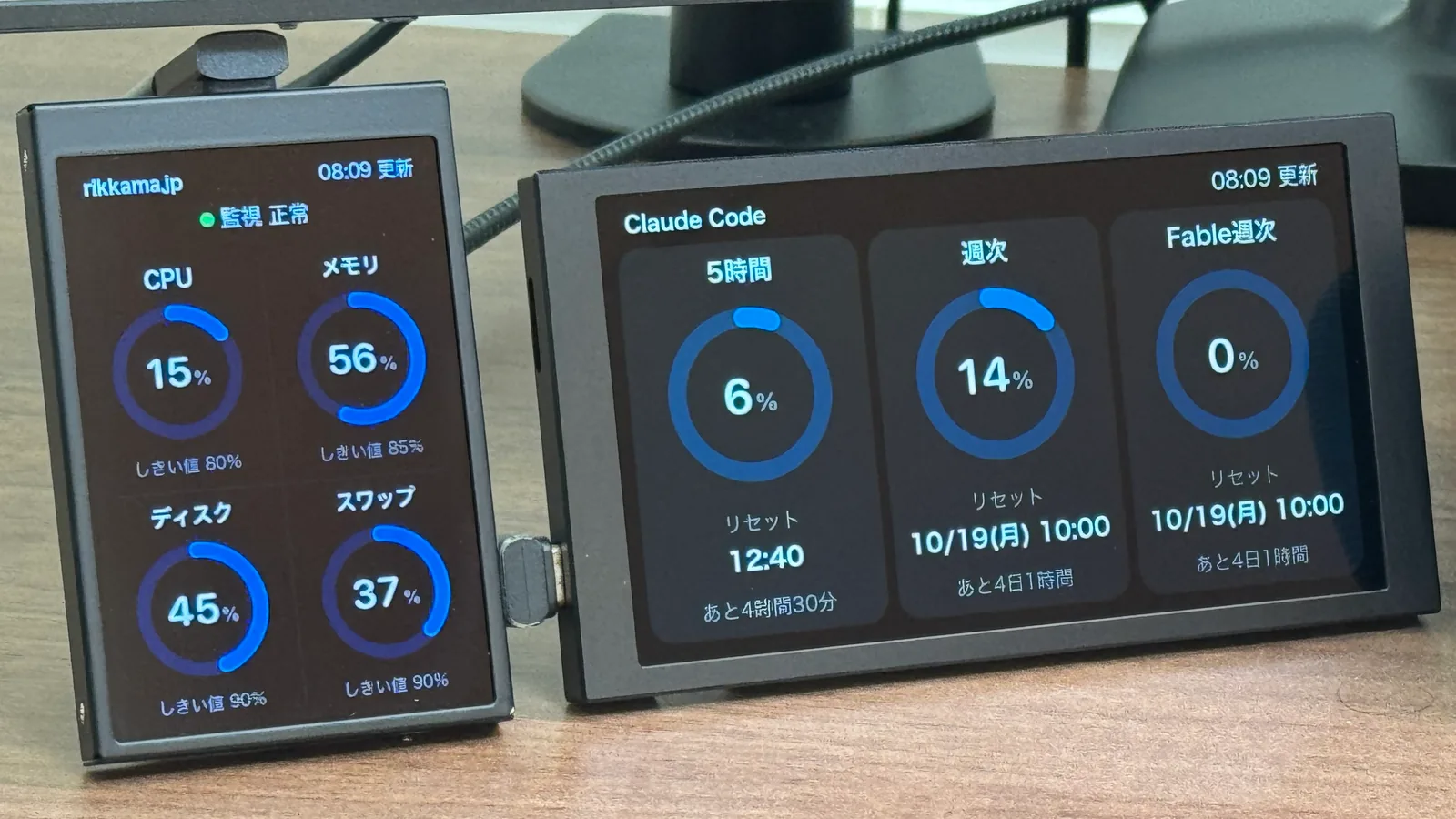 右に横置きの 5.2 インチ。Claude Code の 5 時間・週次・Fable 週次の利用枠が円形のメーターで並ぶ。左に黒く塗装した縦置きの 3.5 インチ。rikkama.jp の CPU・メモリ・ディスク・スワップの使用率が出ている